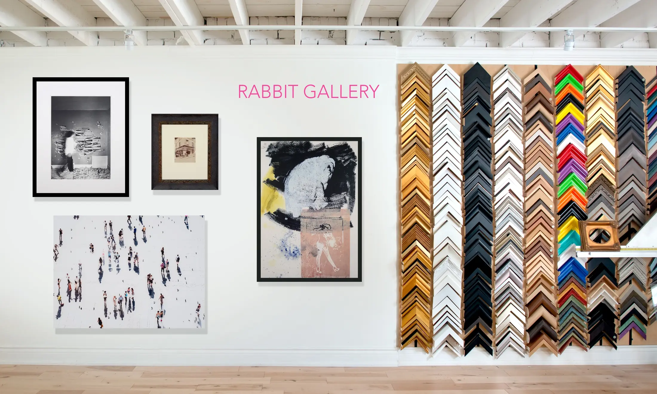 Framed artwork on a white gallery wall beside racks of frame corner samples at Rabbit Gallery, Toronto